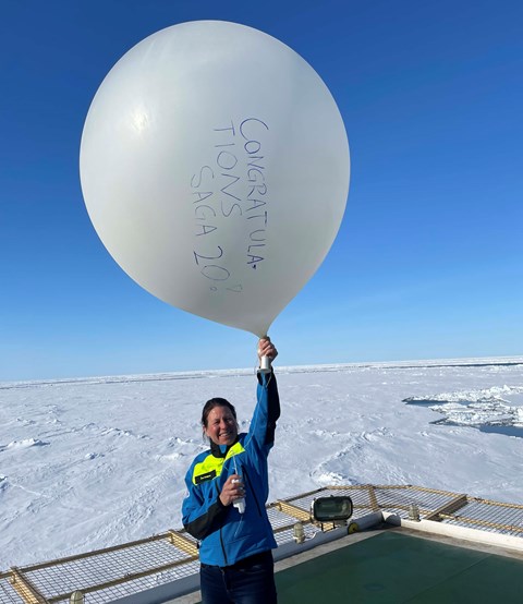  Person in blue and yellow jacket holding up a weather balloon with handwritten text