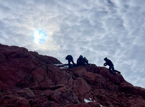 The silhouettes of some people working on a mountain ridge.