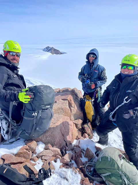 Three people stand on a cliff and smile at the camera.