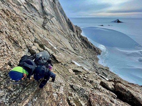 Person som klättrar på en bergsrygg. I bakgrunden syns milsvida glaciärer. 