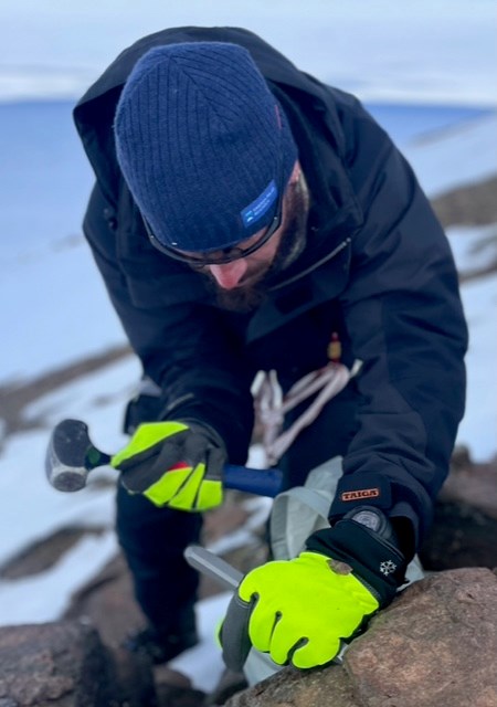 En person håller i en hammare och ett verktyg för att avlägsna en bit sten från klippan. 