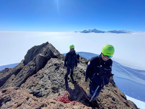 Två personer befinner sig på en bergsrygg inbundna i rep.