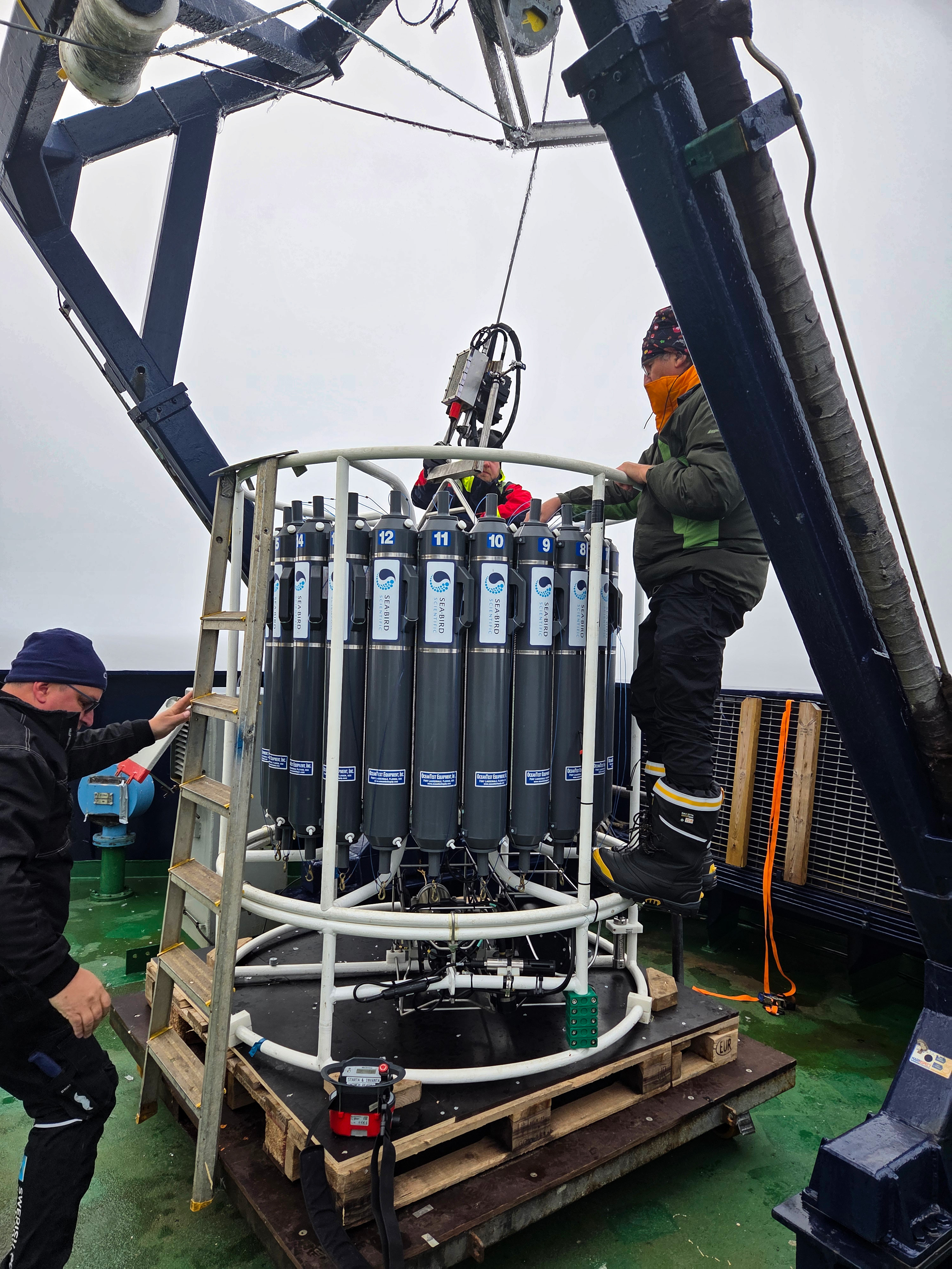 Two technicians prepare a CTD rosette equipped with water-sampling bottles on board Oden.