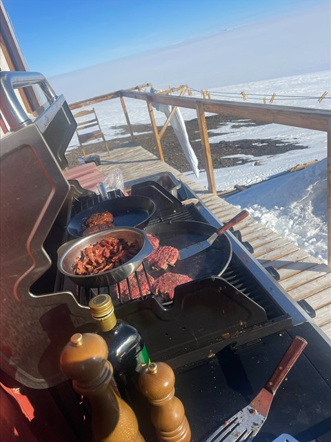 En grill där kött tillagas. I bakgrunden syns de antarktiska vidderna. 
