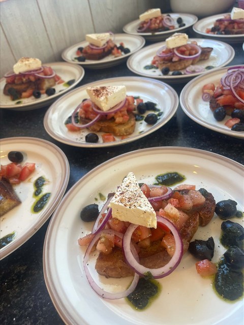 Bread, tomato, feta cheese, red onion and olives laid out on several smaller plates.