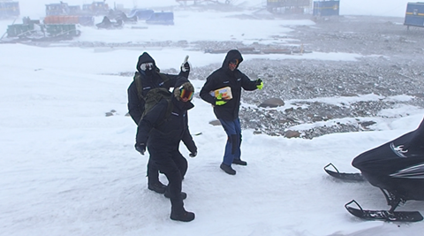 Three people in the station area. They have a hard time withstanding the wind.