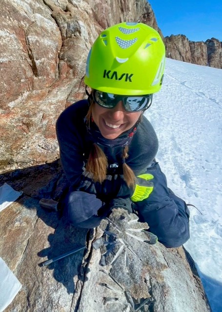 A woman in a yellow helmet holds a stone sample.