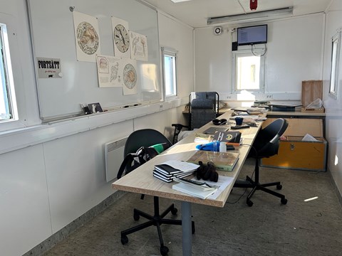En inredd container med vita väggar, whiteboard, bord och kontorsstolar.