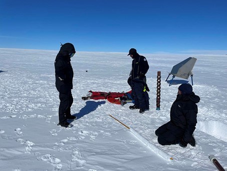 Three persons are standing on the snow and will mount a radar reflector.
