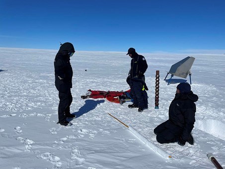 Tre personer står på snön och ska montera en radarreflektor.
