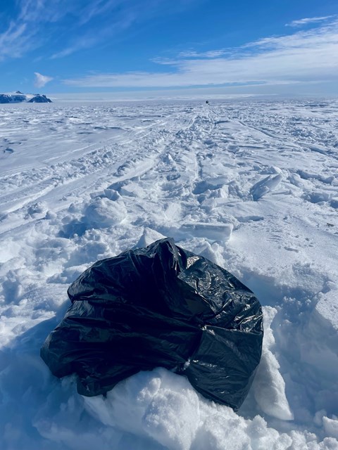 En svart sopsäck ligger på snön. 