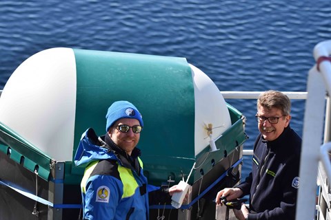 Two people fills a weather balloon. Water is visible in the background.