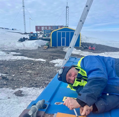 En man i gul och blå jacka arbetar på taket av en container.