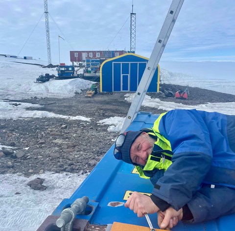 En man i gul och blå jacka arbetar på taket av en container. 