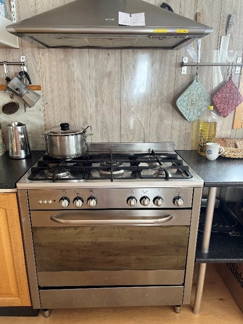 There is a saucepan on the large gas stove, and kitchen accessories hang on the adjacent walls.