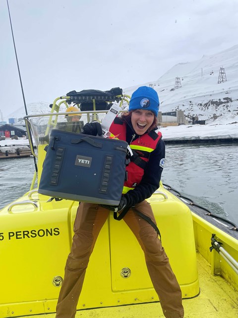 Happy woman standing in a yellow boat and holding a blue bag.