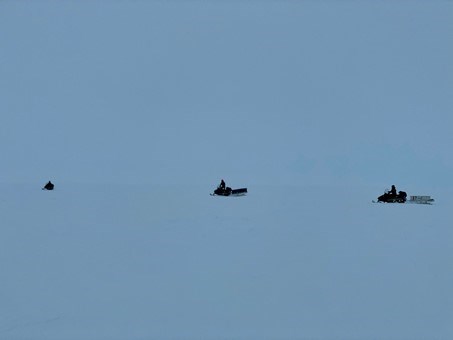 Three snowmobile drivers out on the ice. 