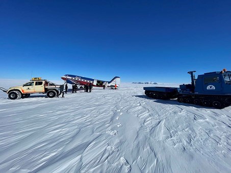 Ett fraktplan har landat på isen. Framför planet står en bil och en bandvagn.